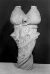 Foliated terminal of a Roman shaft: above a series of carved spirals terminating in acanthus leaves are two stylised pine cones flanked by a foliate scroll. The tops of the pine cones are smoothed forming flat surfaces. 