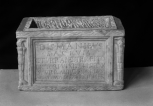 A Roman funerary urn (cinerarium) with a rectangular name plate between lighted torches